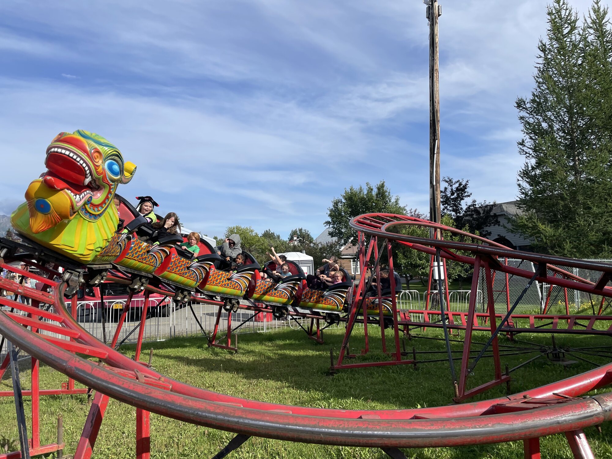 Kids riding a colorful dragon roller coaster at a summer carnival.